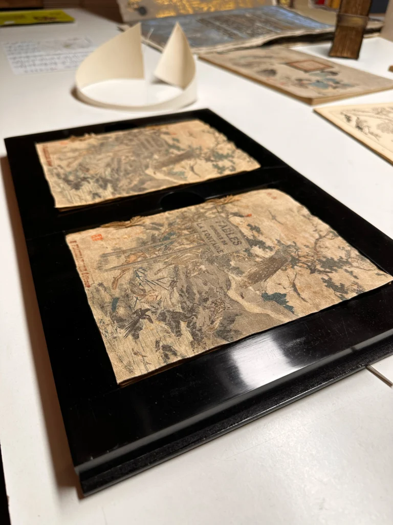 Deux éléments de couverture anciens disposés dans une boîte de conservation noire laquée.