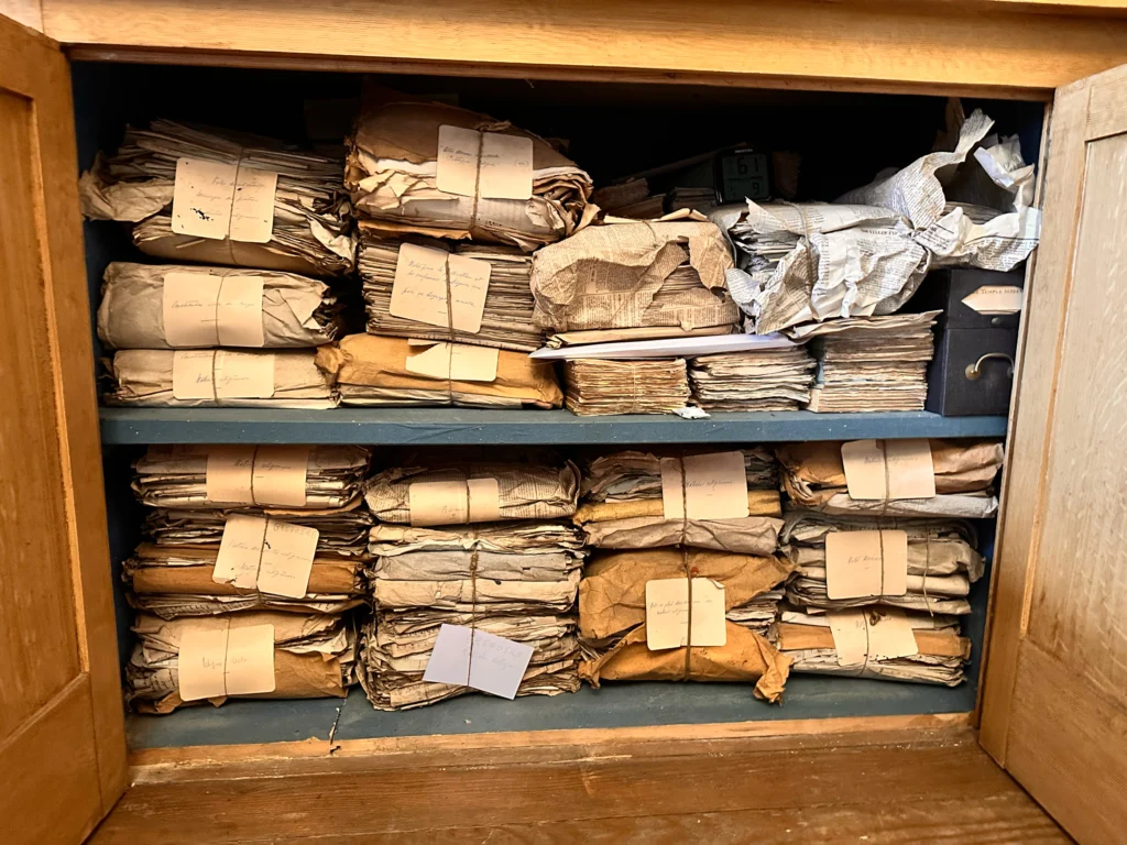 Liasses de documents anciens rangées sur les étagères d’une armoire en bois.