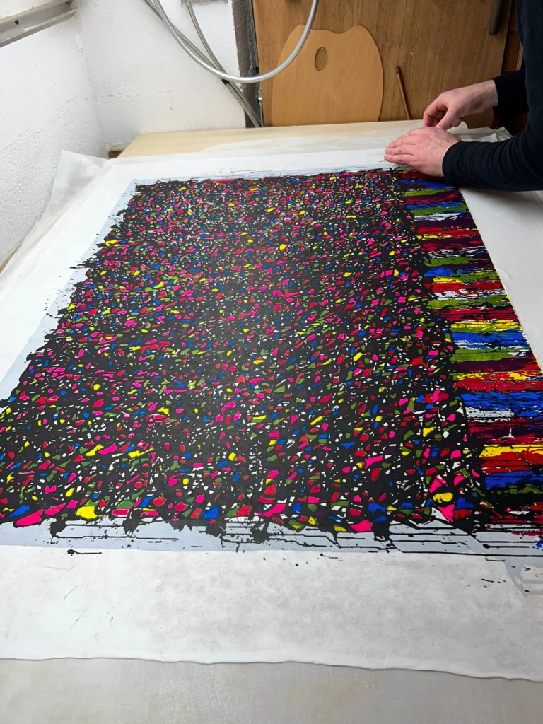 Œuvre graphique multicolore à plat sur une table, avec des mains maintenant son bord.