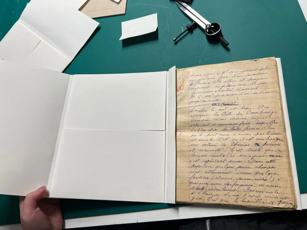 Feuillet manuscrit placé dans une pochette de conservation à reliure, ouverte sur une table de travail.