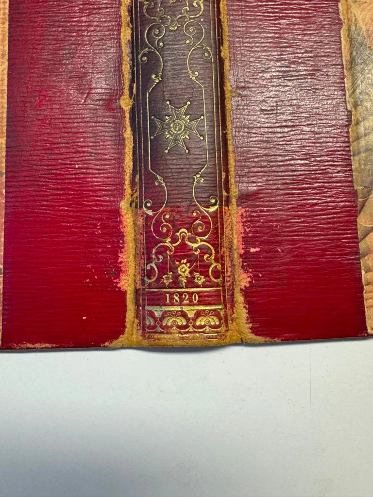 Détail du dos doré d’une reliure rouge, sans étiquette de classement.