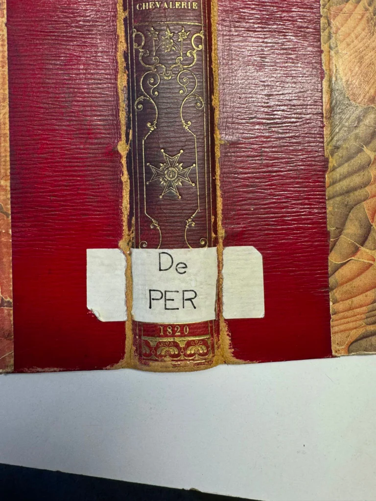 Étiquette de classement en papier apposée sur le dos doré d’une reliure rouge.