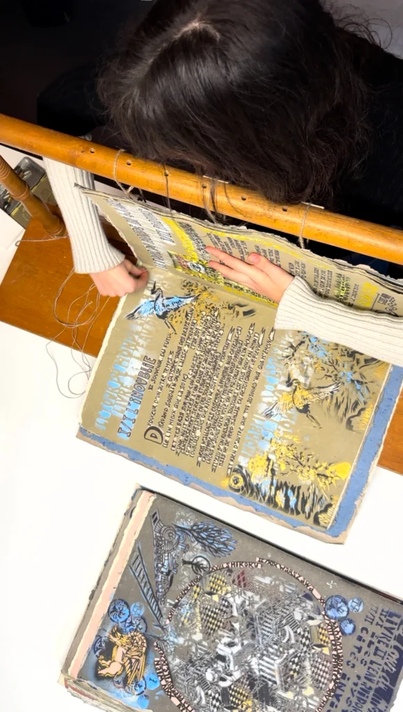 Couture d’un cahier d’un livre en pochoir, ouvert sur un établi.