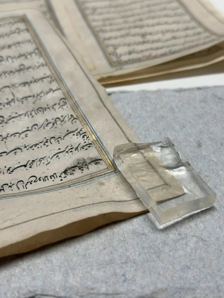 Page de manuscrit perse du XVIIIe siècle maintenue à plat sous un poids de verre.